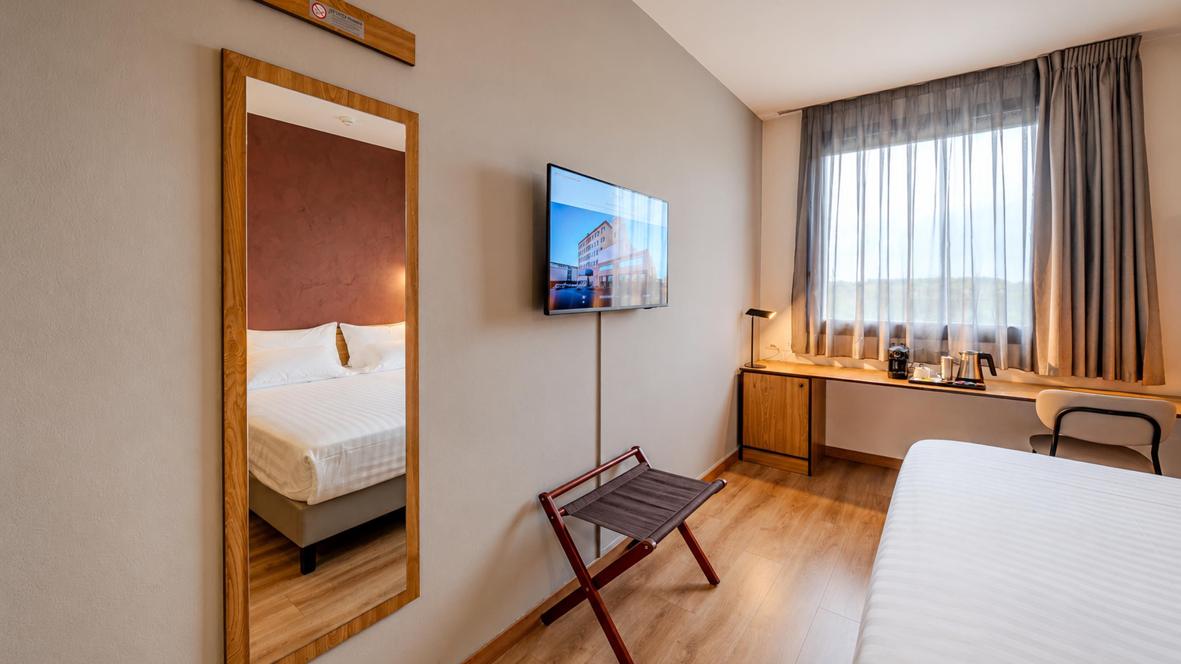 A hotel room with a bed, a desk, a chair, a television, and a window with curtains.