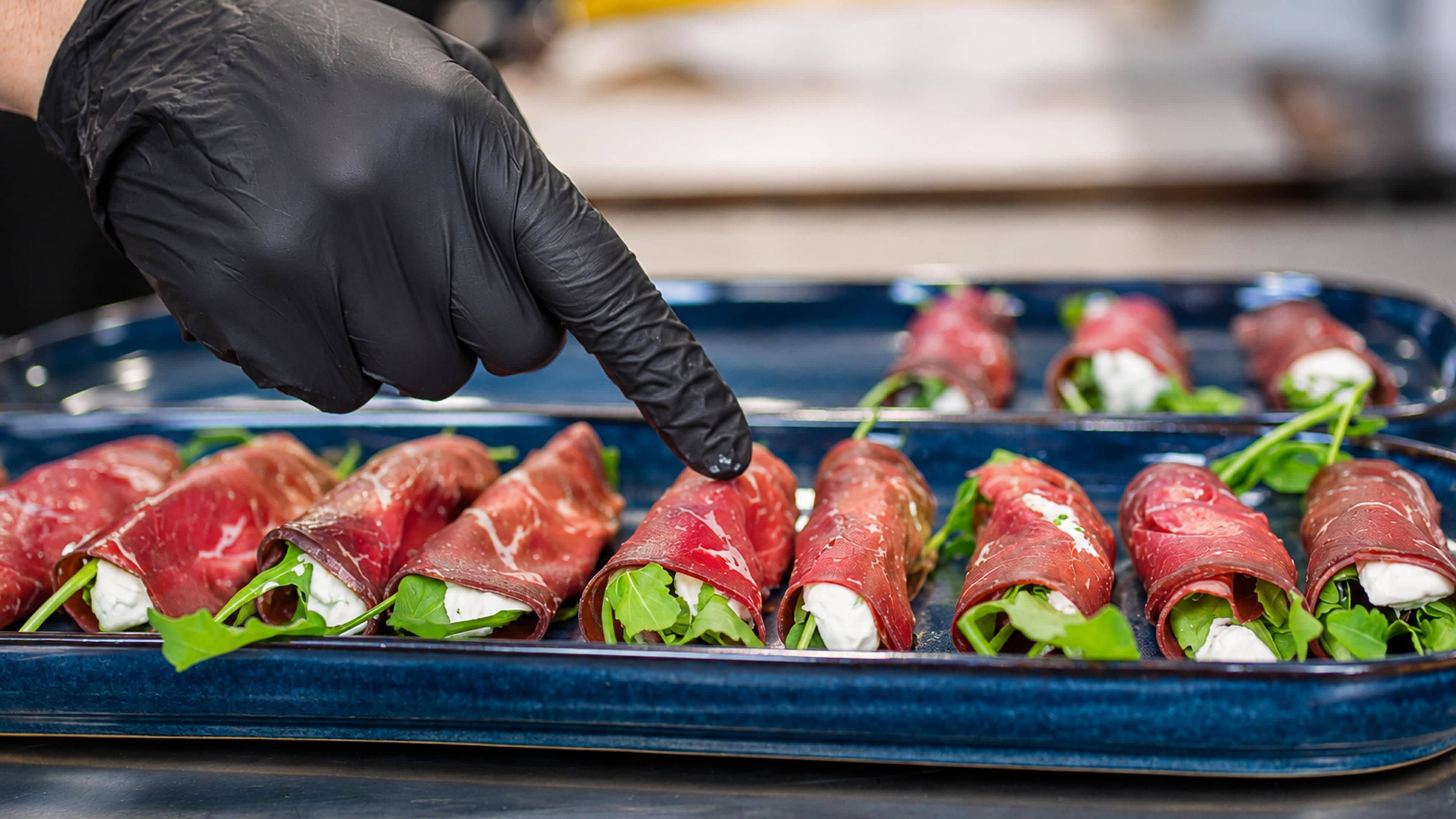 A tray of food items, possibly appetizers, with a gloved hand placing a piece on it.