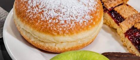 Une assiette de petit-déjeuner comprenant des œufs brouillés, du bacon, un beignet, une part de tarte, un verre de jus d’orange et une pomme.