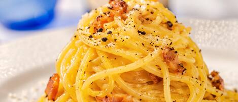 A plate of spaghetti with a creamy sauce, garnished with black pepper and cheese, with a bottle and glass in the background.