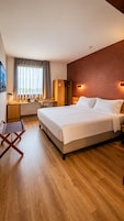 Una habitación de hotel con una cama grande, un escritorio con una silla, un armario y una ventana con cortinas.