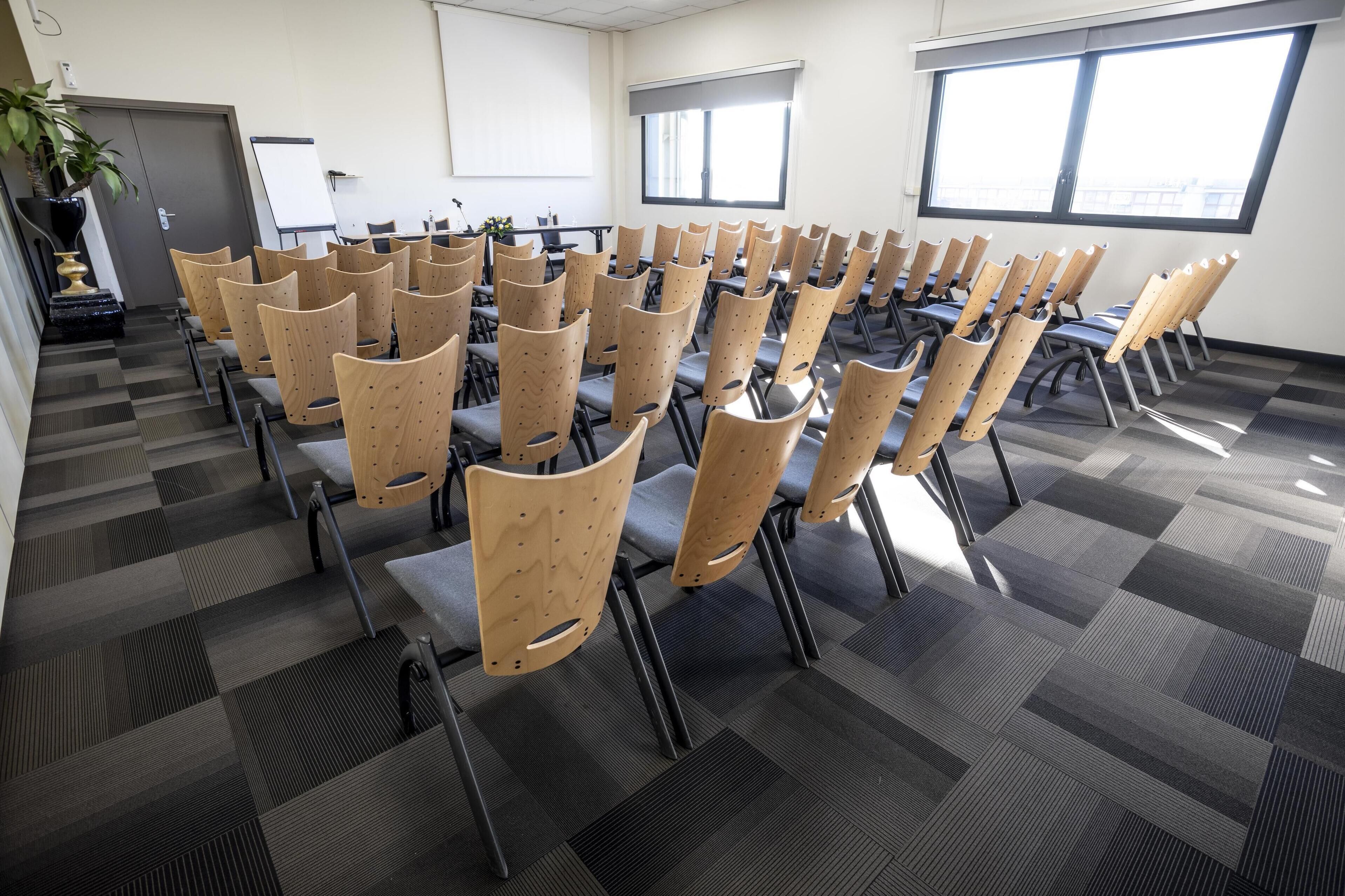 Un salón de conferencias con filas de sillas, una pizarra y un ventanal grande.