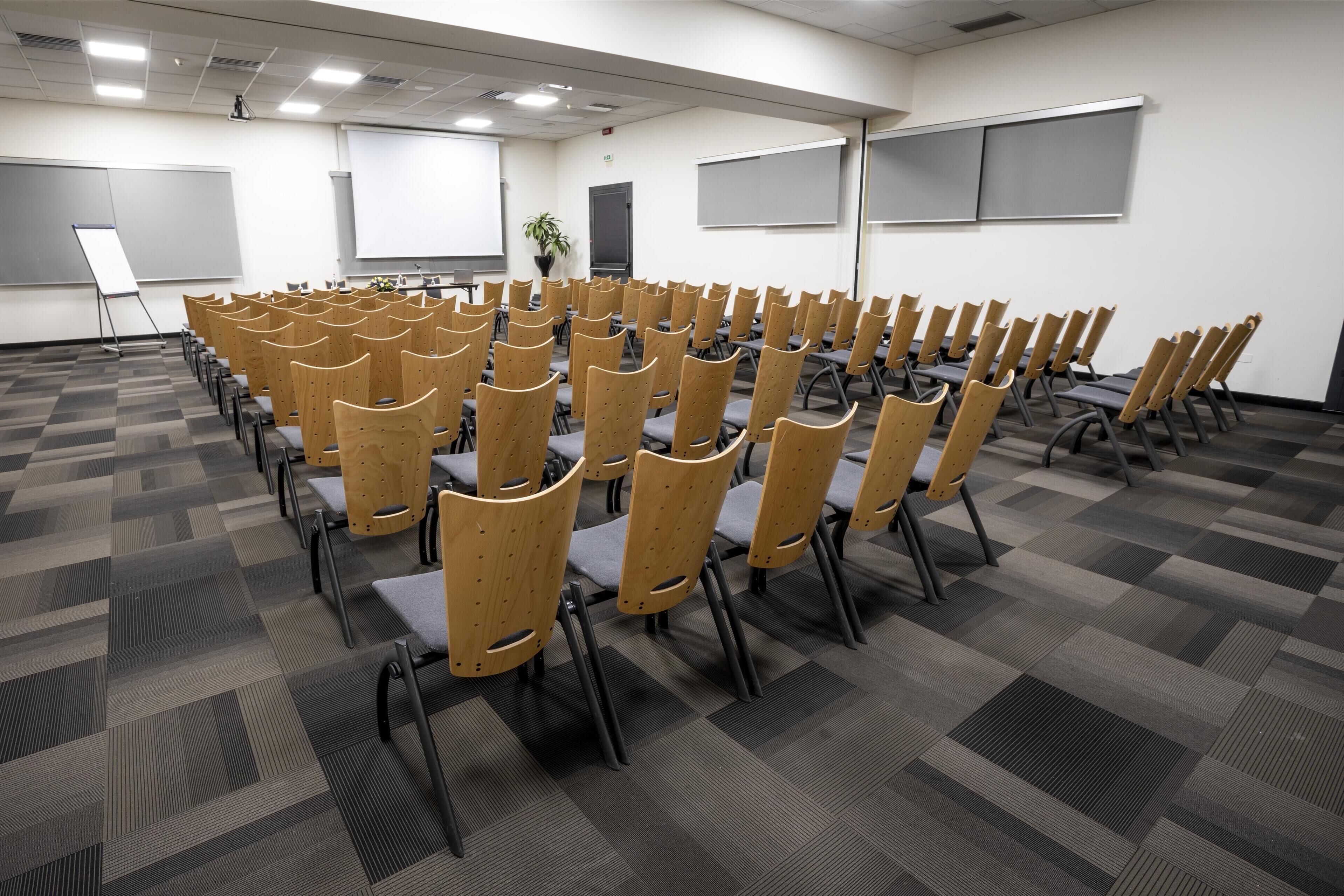 Un salón de conferencias con filas de sillas de madera y piso alfombrado.