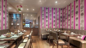 A restaurant with booths and tables, wooden floors, and a floral wall pattern. - Masséna Hôtel (Paris)