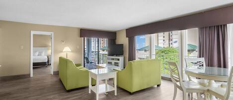 Une chambre d’hôtel comprenant un lit, une télévision, une table à manger avec des chaises et un balcon donnant sur des immeubles.