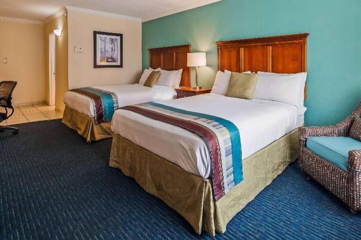 Habitación de hotel con dos camas, una silla, una lámpara y un cuadro en la pared.