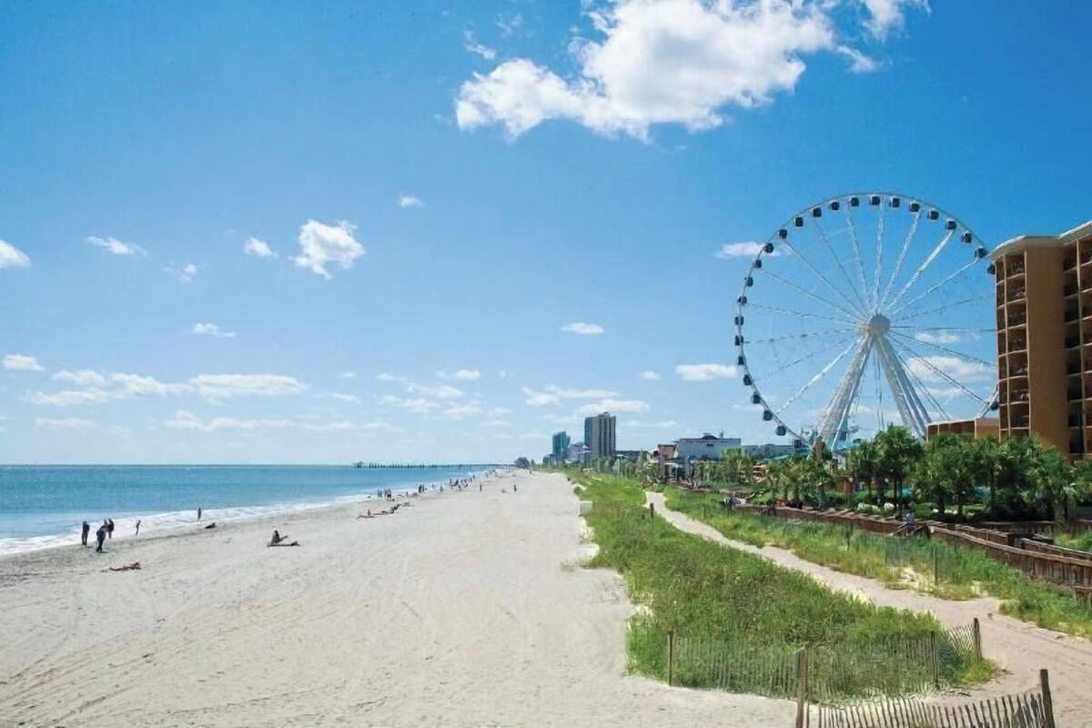 A beach with a large Ferris wheel, a sandy shore, and a path along the beach.