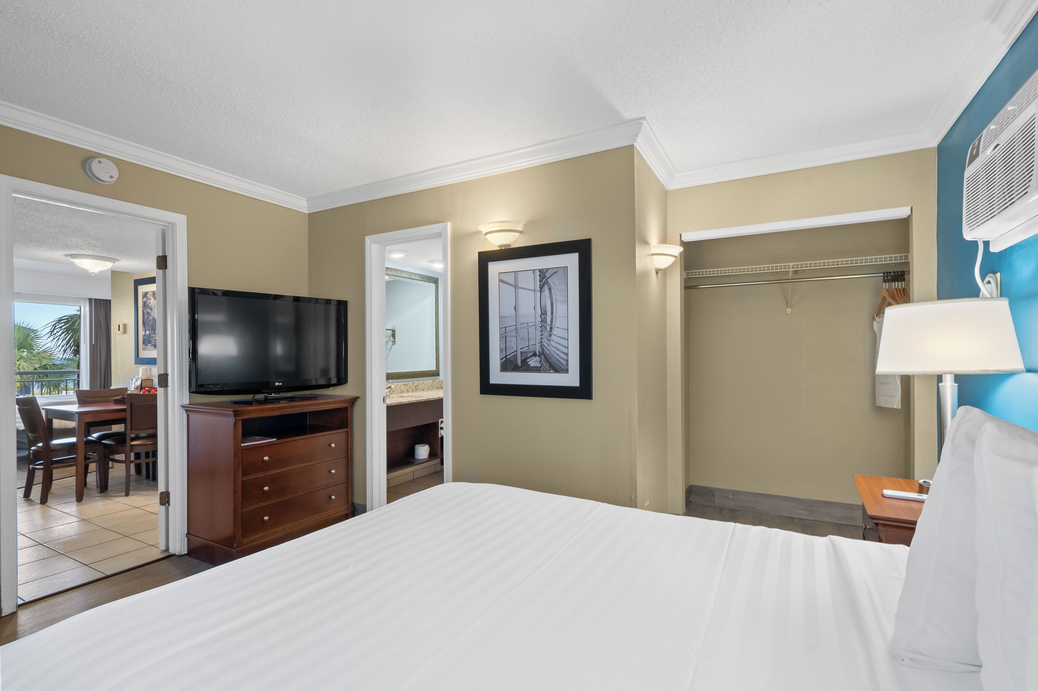 A hotel room with a bed, a TV, a desk with a chair, a wardrobe, and a bathroom visible through an open door.