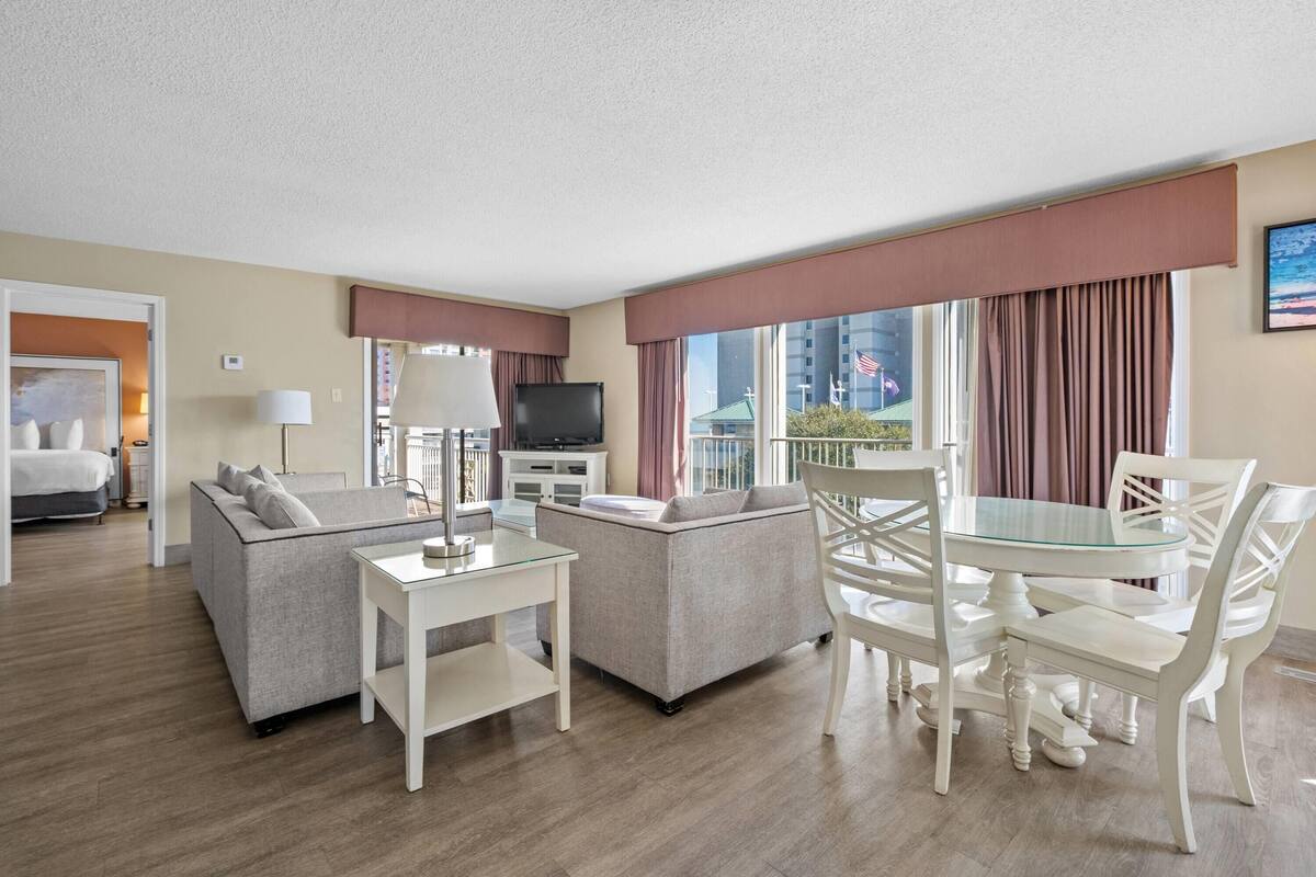 Habitación de hotel con sofá, mesa de vidrio, televisión y vista panorámica de la ciudad.