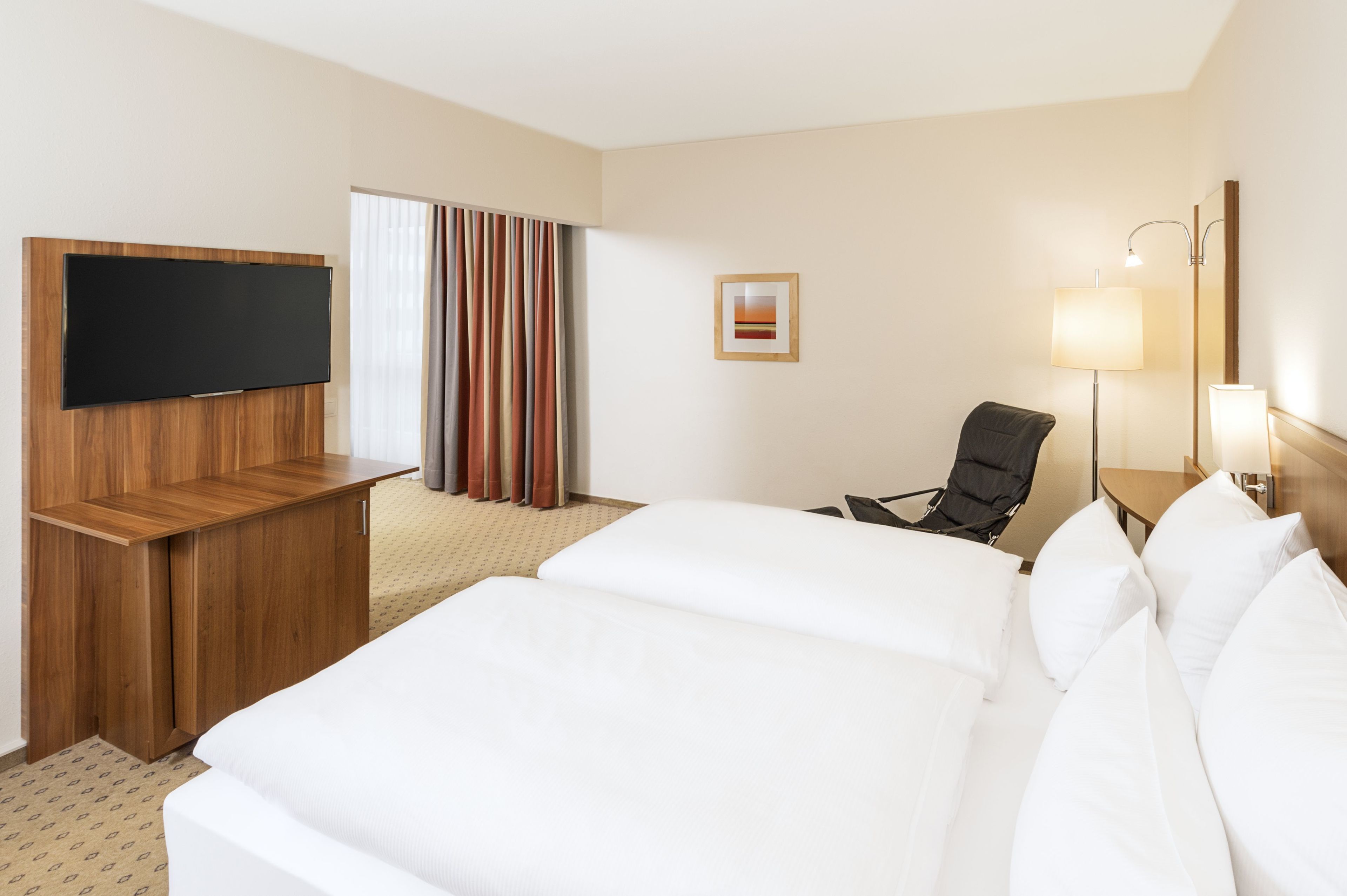 A hotel room with two beds, a flat-screen TV, a desk, a chair, a lamp, and a framed picture on the wall.