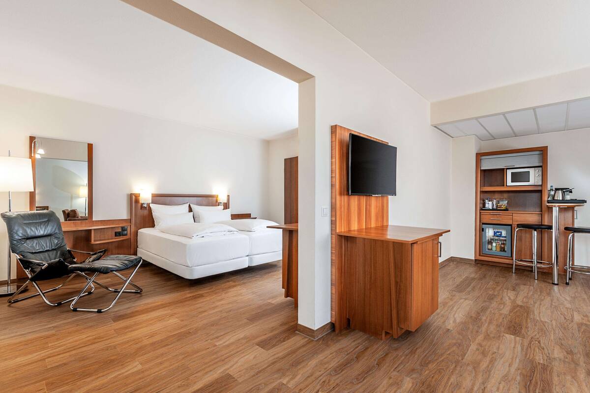 A modern hotel room with a bed, a desk, a TV, a microwave, and a minibar.