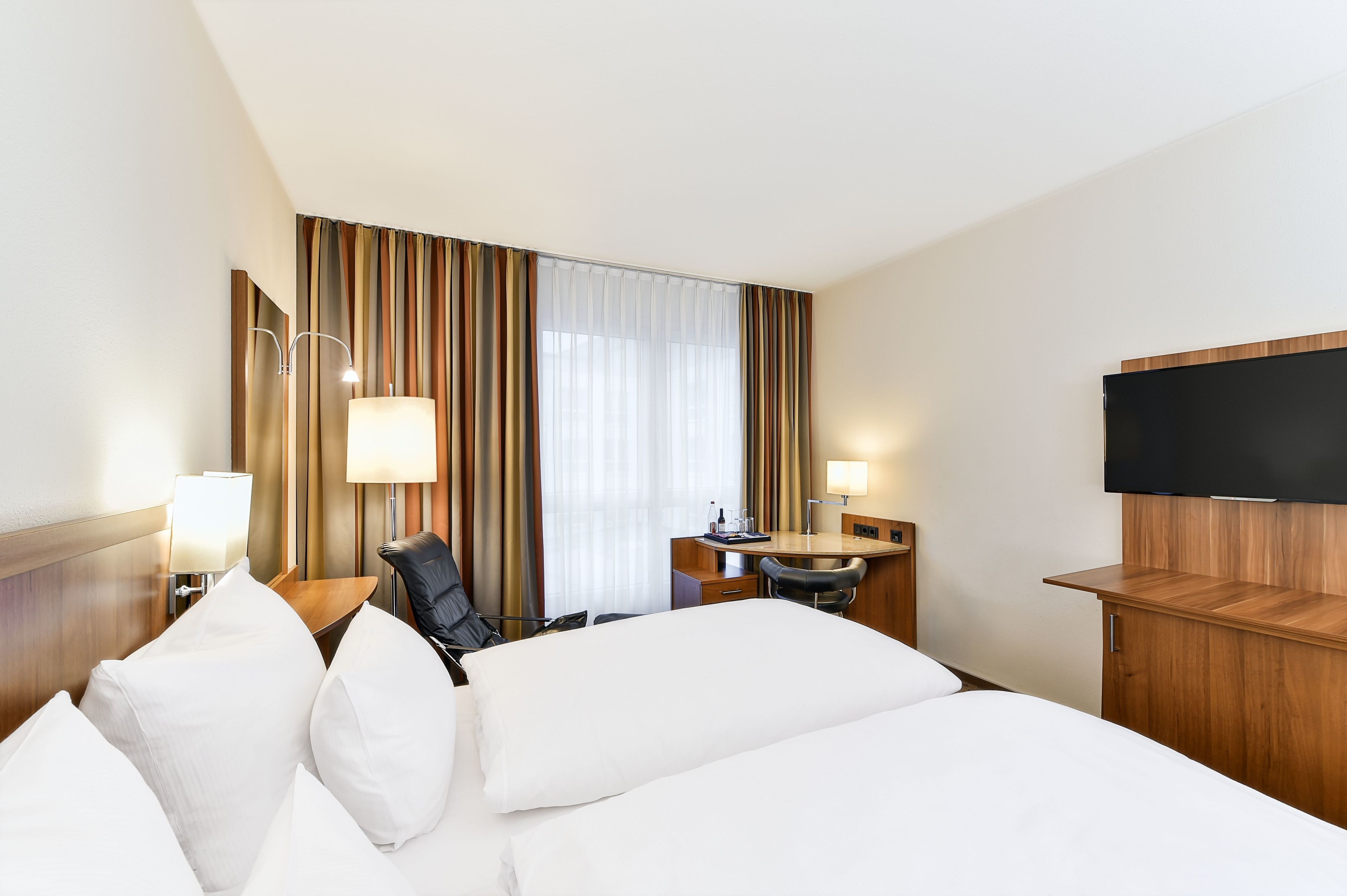 Une chambre d’hôtel équipée d’un lit, d’un bureau, d’une chaise, d’une télévision et d’une fenêtre avec des rideaux.