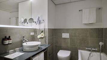A modern bathroom with a large mirror, a round sink, a toilet, and a shower area.