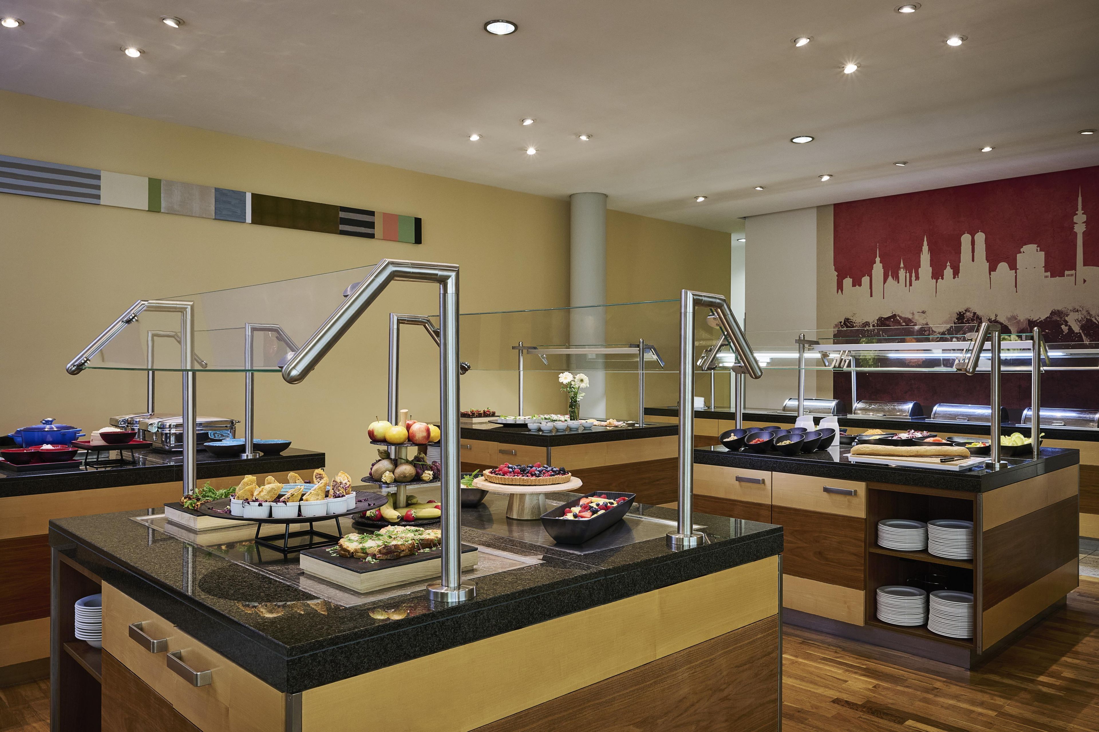 A buffet area with various food items and a city skyline mural on the wall.