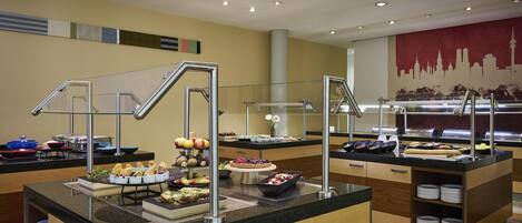 A buffet area with various food items and a city skyline mural on the wall.