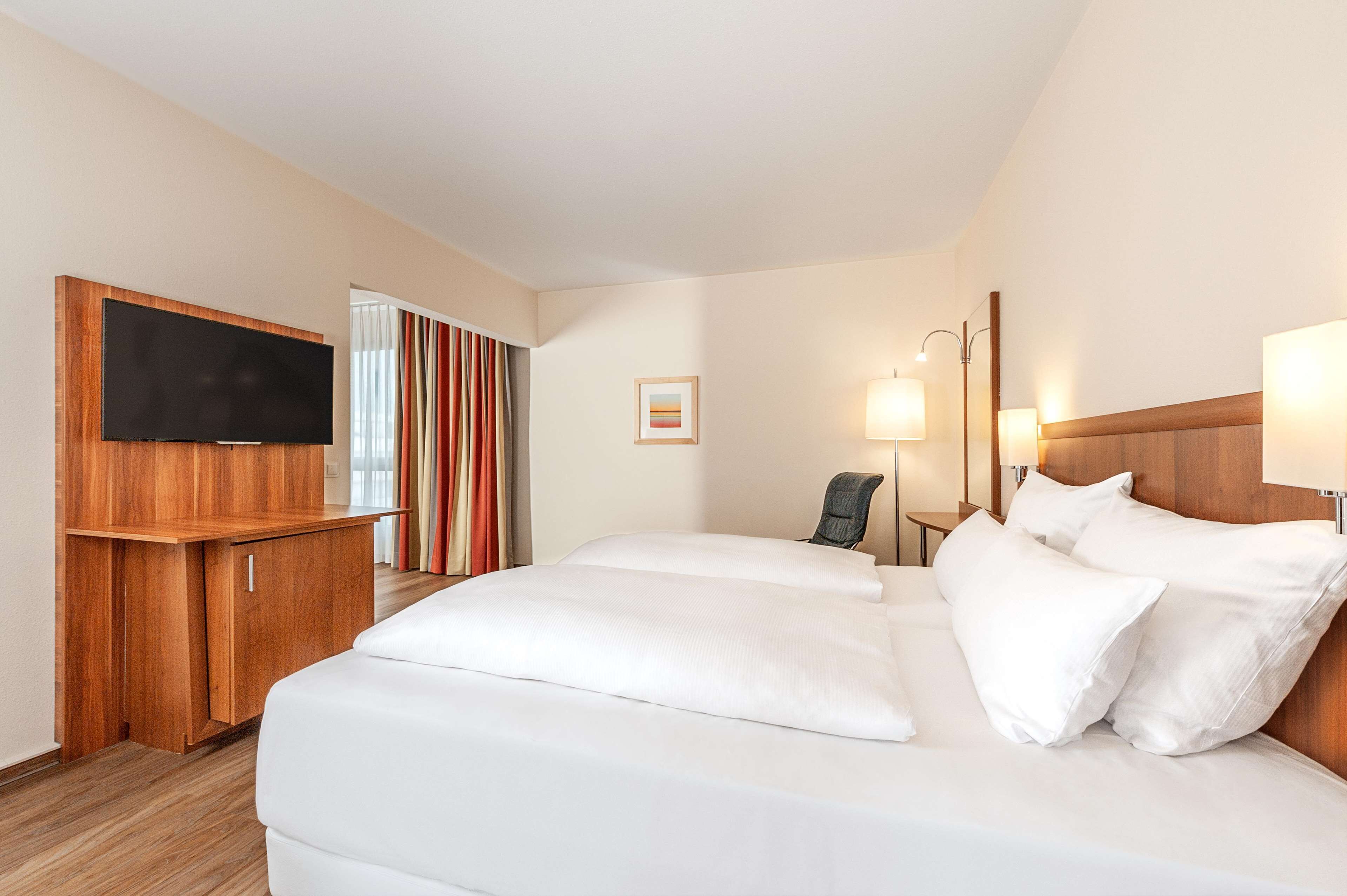 Habitación de hotel con una cama grande, un televisor en un mueble de madera, un escritorio y una silla.