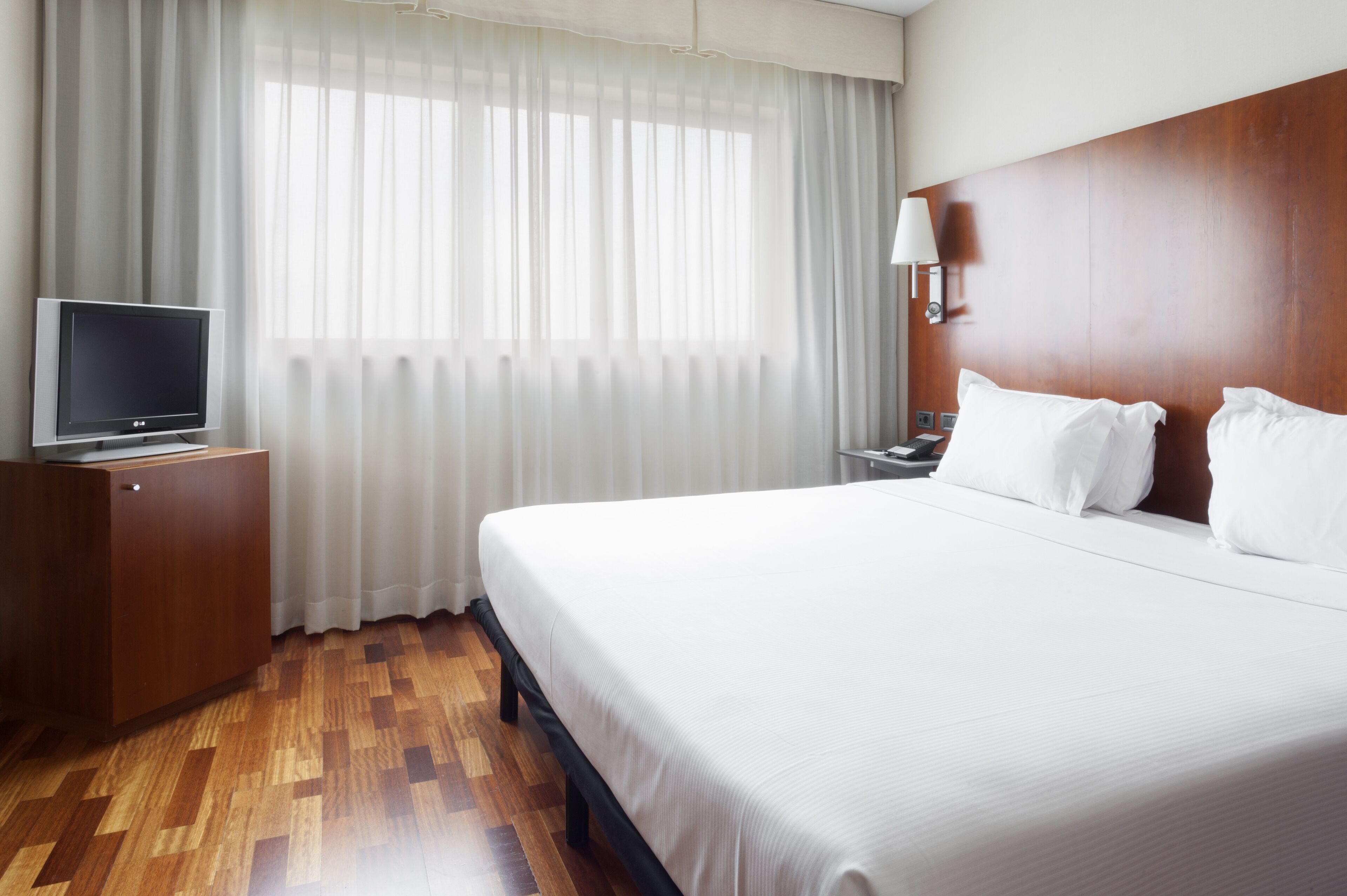 A hotel room with a large bed, a TV on a wooden cabinet, a nightstand, and a lamp.