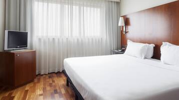 A hotel room with a large bed, a TV on a wooden cabinet, a nightstand, and a lamp.