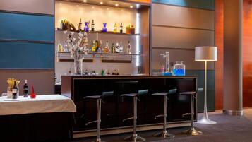 Een bar met een witte tafel, meerdere stoelen en planken met flessen en bloemen.