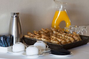Un bufé de desayuno con pasteles, tazas de café y una jarra de jugo de naranja.