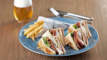 Un plato con un sándwich y papas fritas, una jarra de cerveza y cubiertos sobre una mesa de madera.
