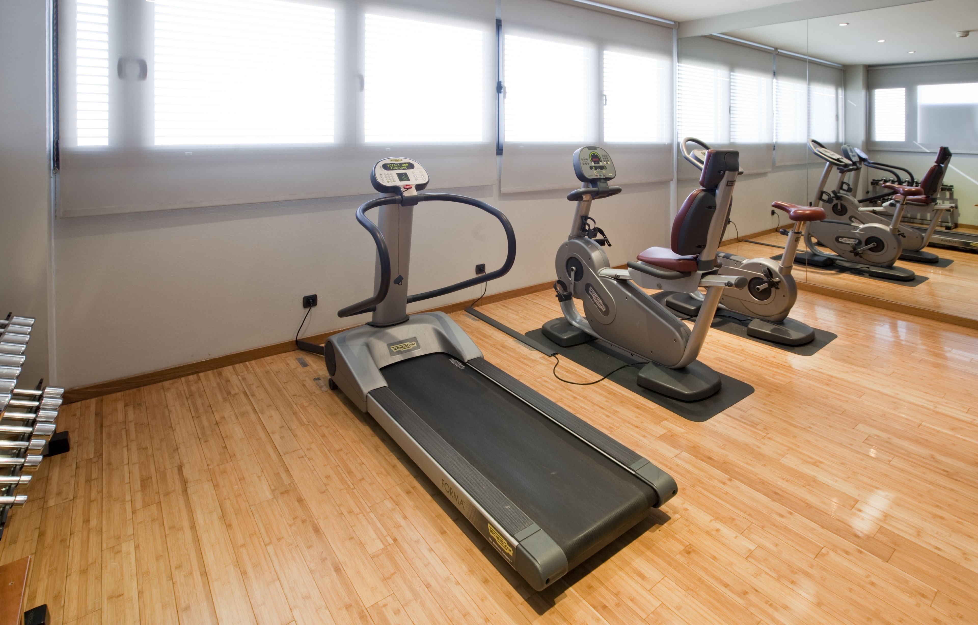Un gimnasio con cintas de correr, bicicletas estáticas y un espejo grande.