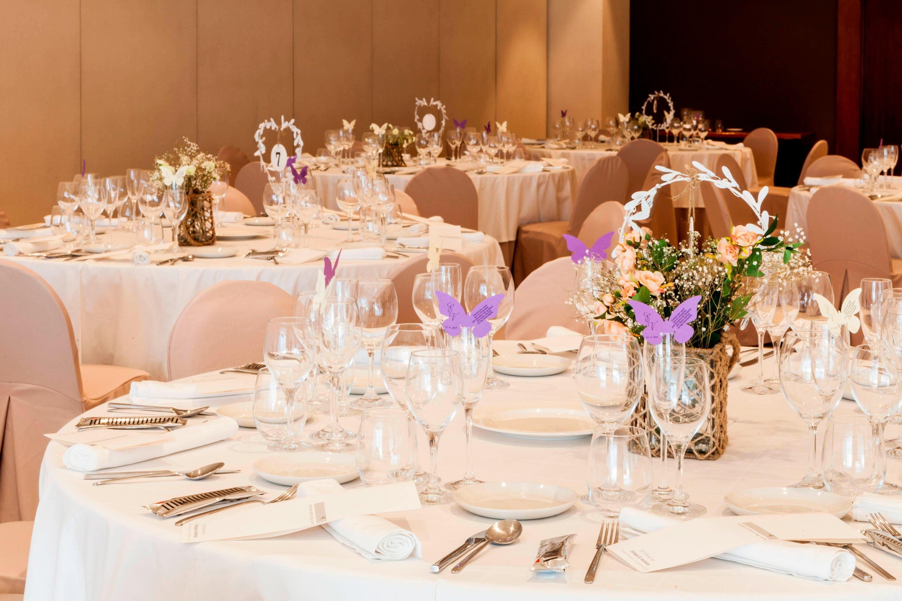 A banquet hall with round tables set for a formal event, each table adorned with white tablecloths, silverware, and glassware.