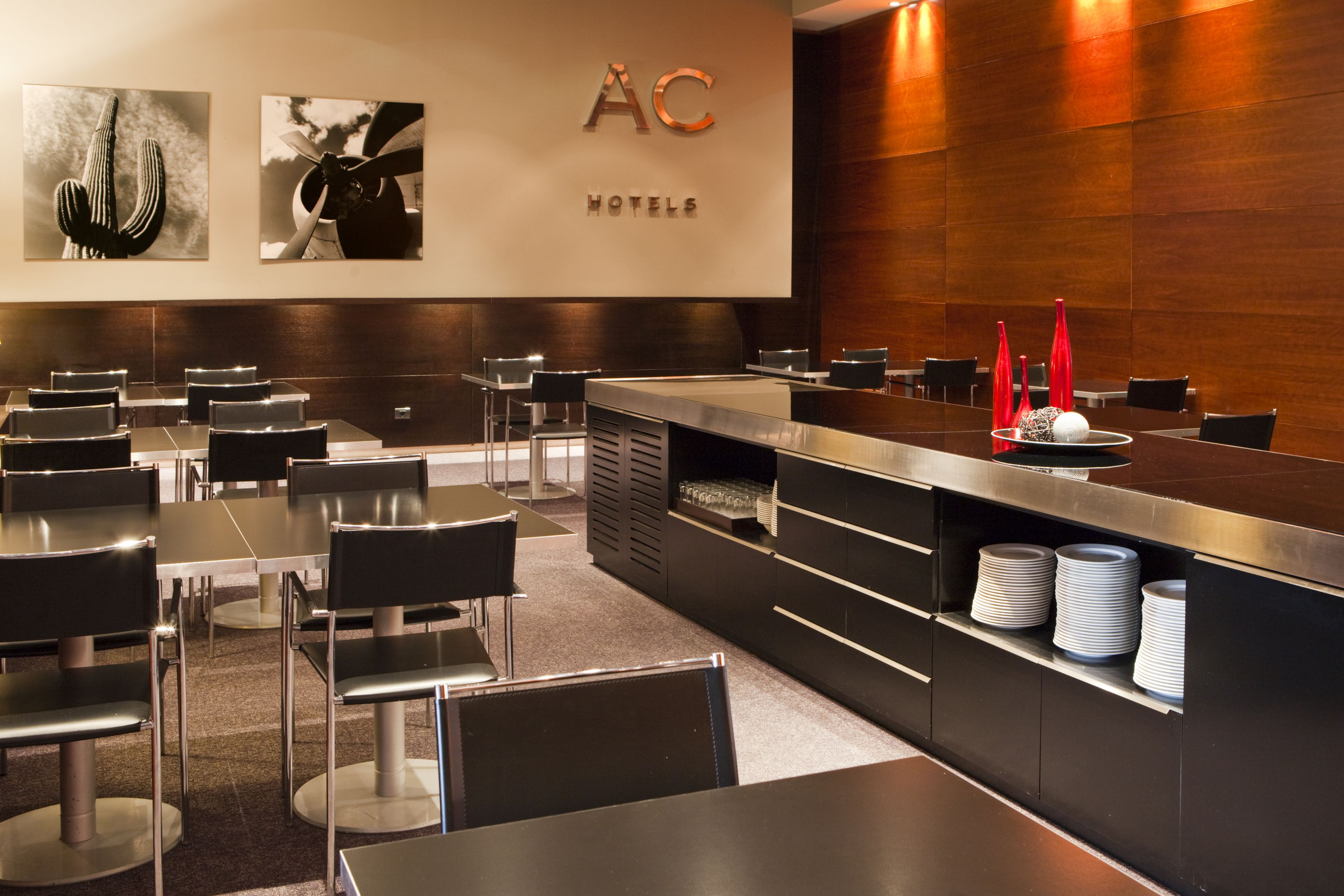 A modern hotel lobby with a reception desk, black chairs, and a counter with stacked plates.