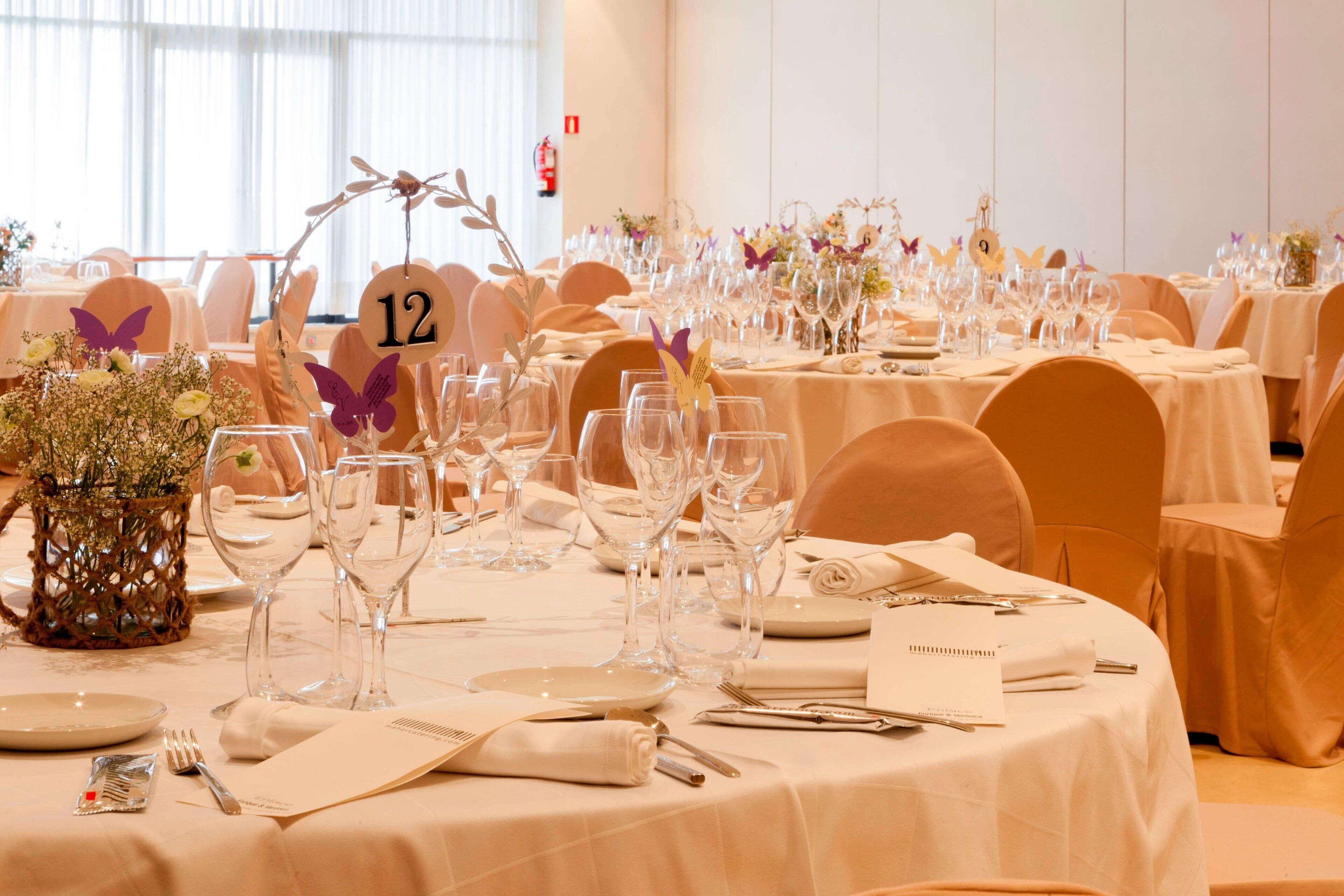 Un salón de banquetes con mesas redondas dispuestas para un evento formal, tarjetas de lugar numeradas y centros de mesa florales.