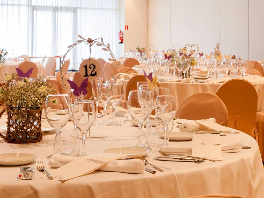 Un salón de banquetes con mesas redondas dispuestas para un evento formal, tarjetas de lugar numeradas y centros de mesa florales.