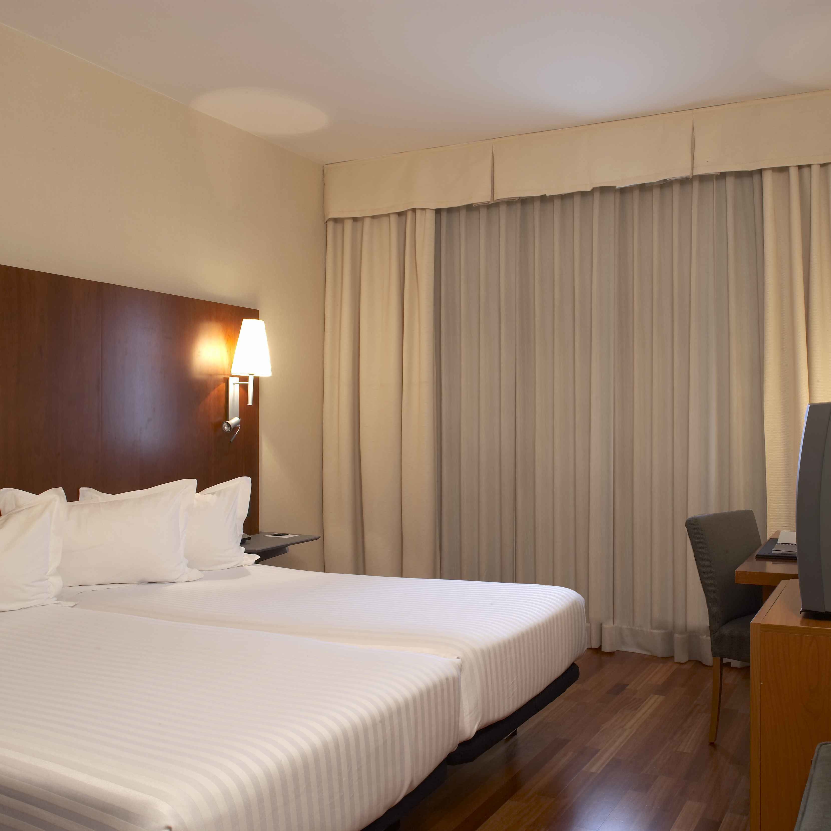 Een hotelkamer met twee bedden, een bureau met stoel, een televisie en een raam met gordijnen.