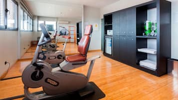 Une salle de sport moderne équipée de machines de cardio, d’un banc d’exercice rouge et d’un meuble de rangement noir avec des étagères.