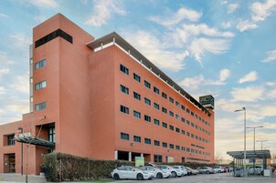 Un hotel de varios pisos con fachada de ladrillo rojo, múltiples ventanas y un estacionamiento con varios automóviles.