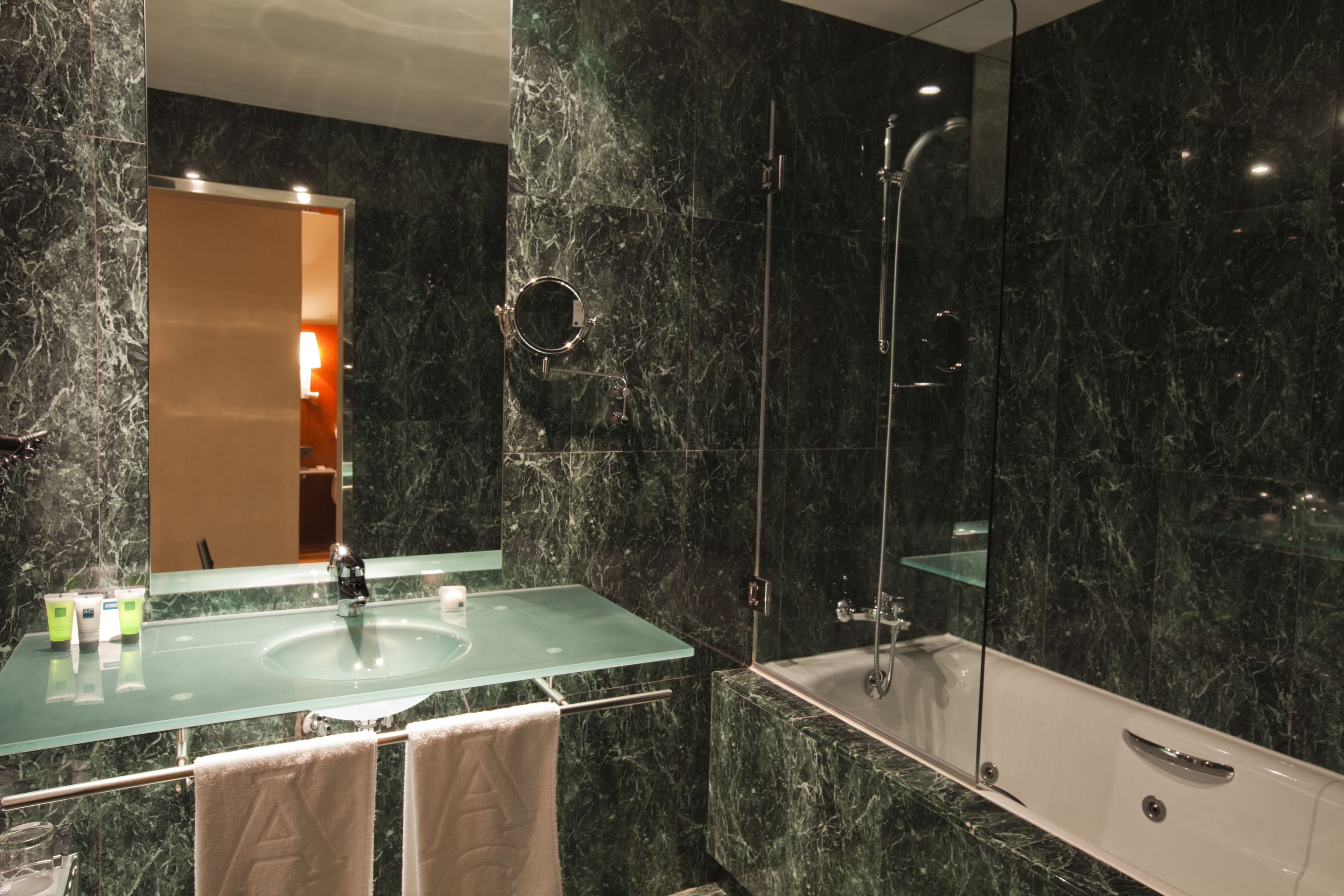 Un baño moderno con un lavamanos de vidrio, una bañera y un espejo grande.