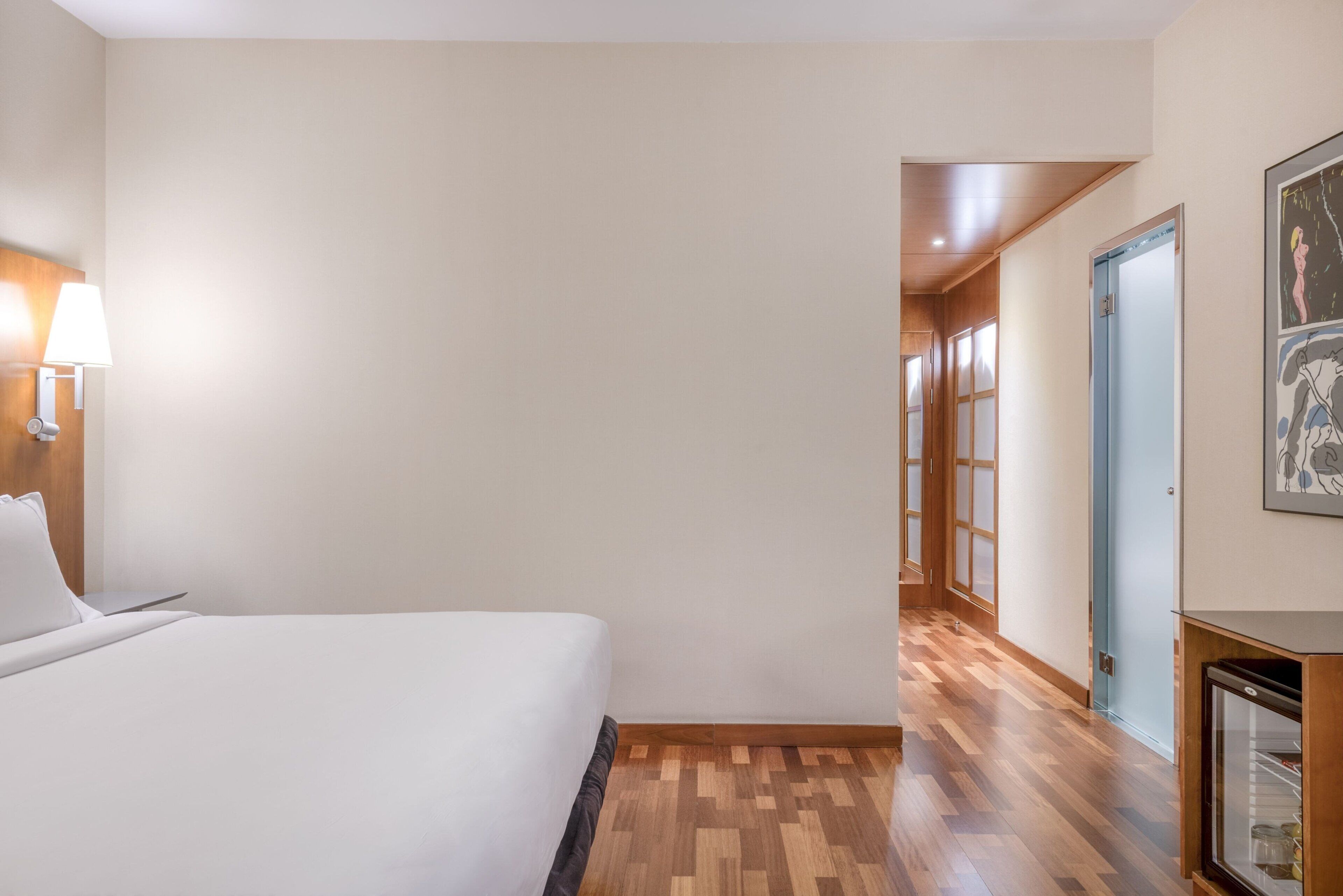 A hotel room with a bed, a nightstand, a lamp, and a wooden floor.