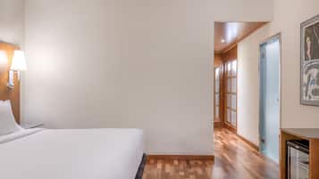 A hotel room with a bed, a nightstand, a lamp, and a wooden floor.