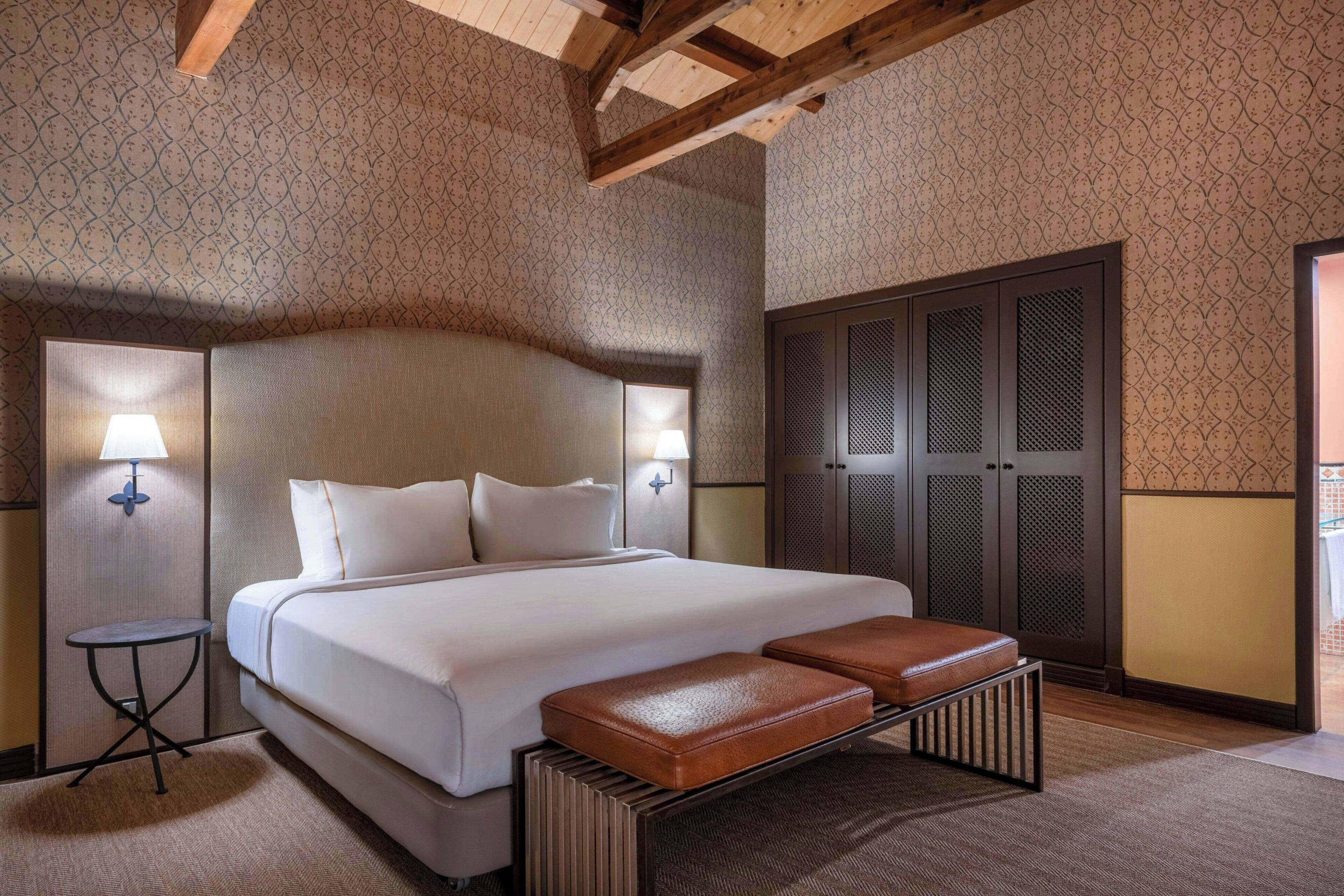 Une chambre d’hôtel avec un grand lit, deux lampes de chevet, une armoire et un banc.