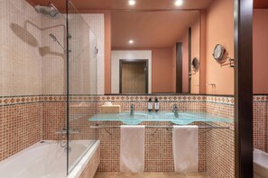 A bathroom with a glass-enclosed shower, two sinks with glass tops, and a bathtub.