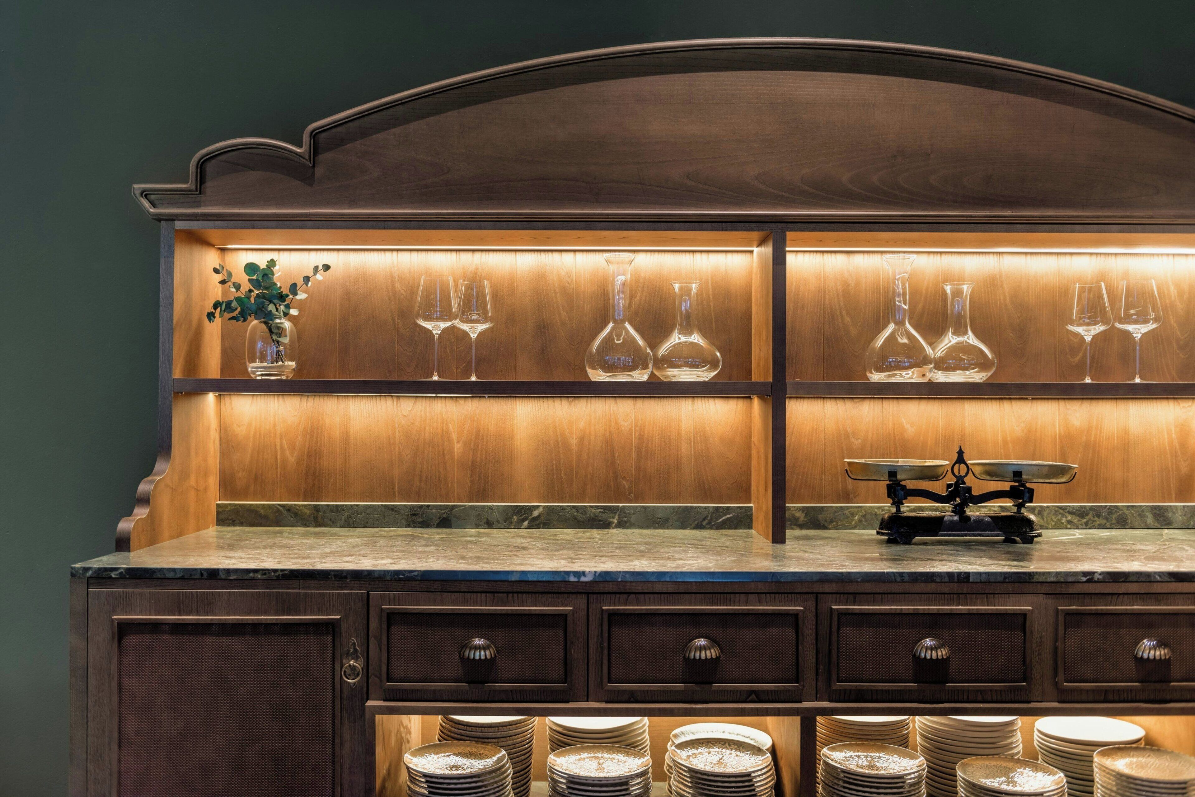 Una cocina con armarios de madera, encimera de mármol y una estantería con copas y botellas de vino.