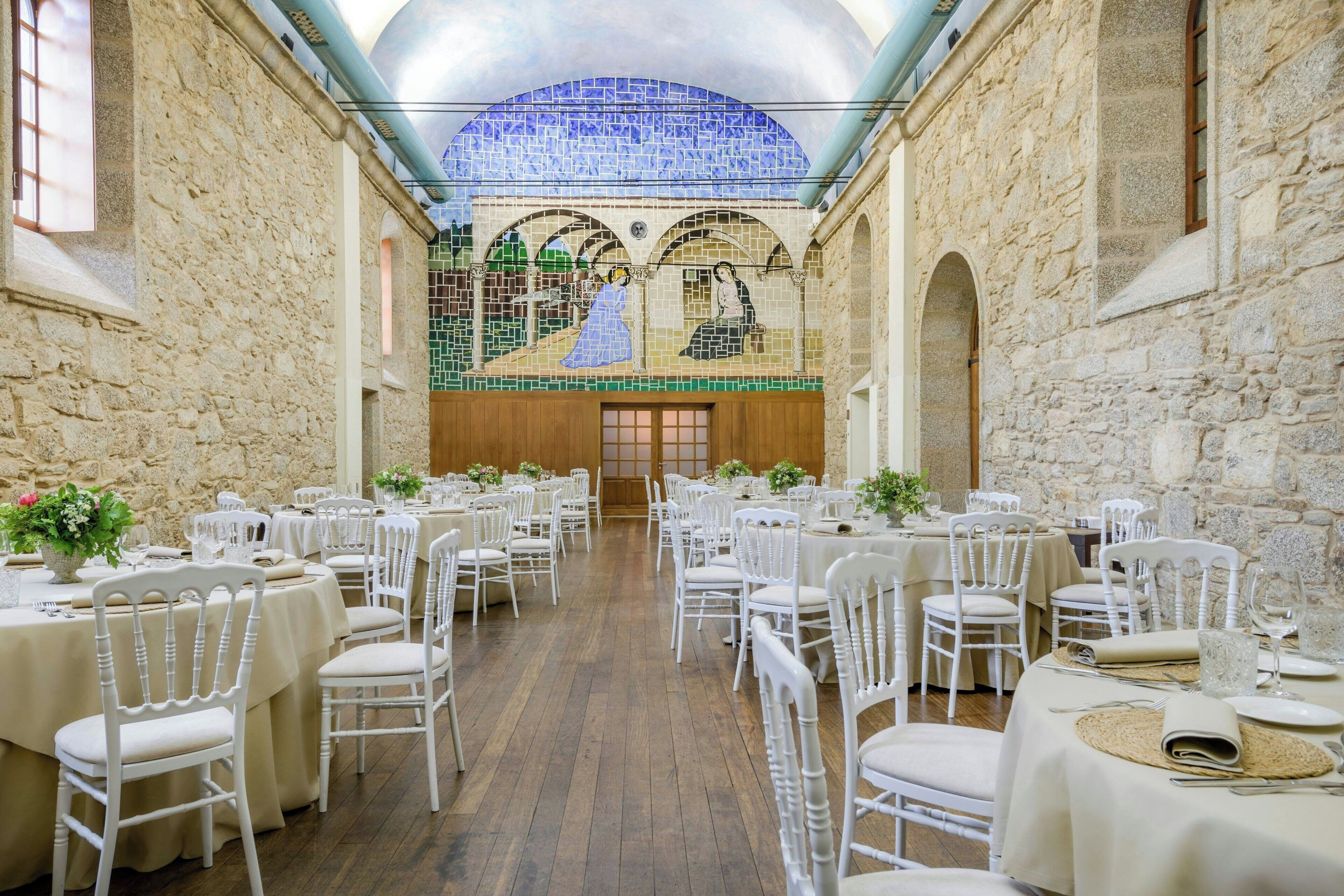 A banquet hall with round tables, white chairs, and a mosaic ceiling.