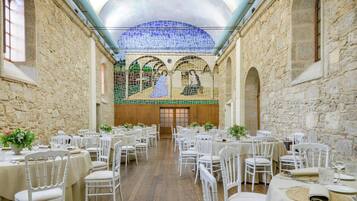 A banquet hall with round tables, white chairs, and a mosaic ceiling.