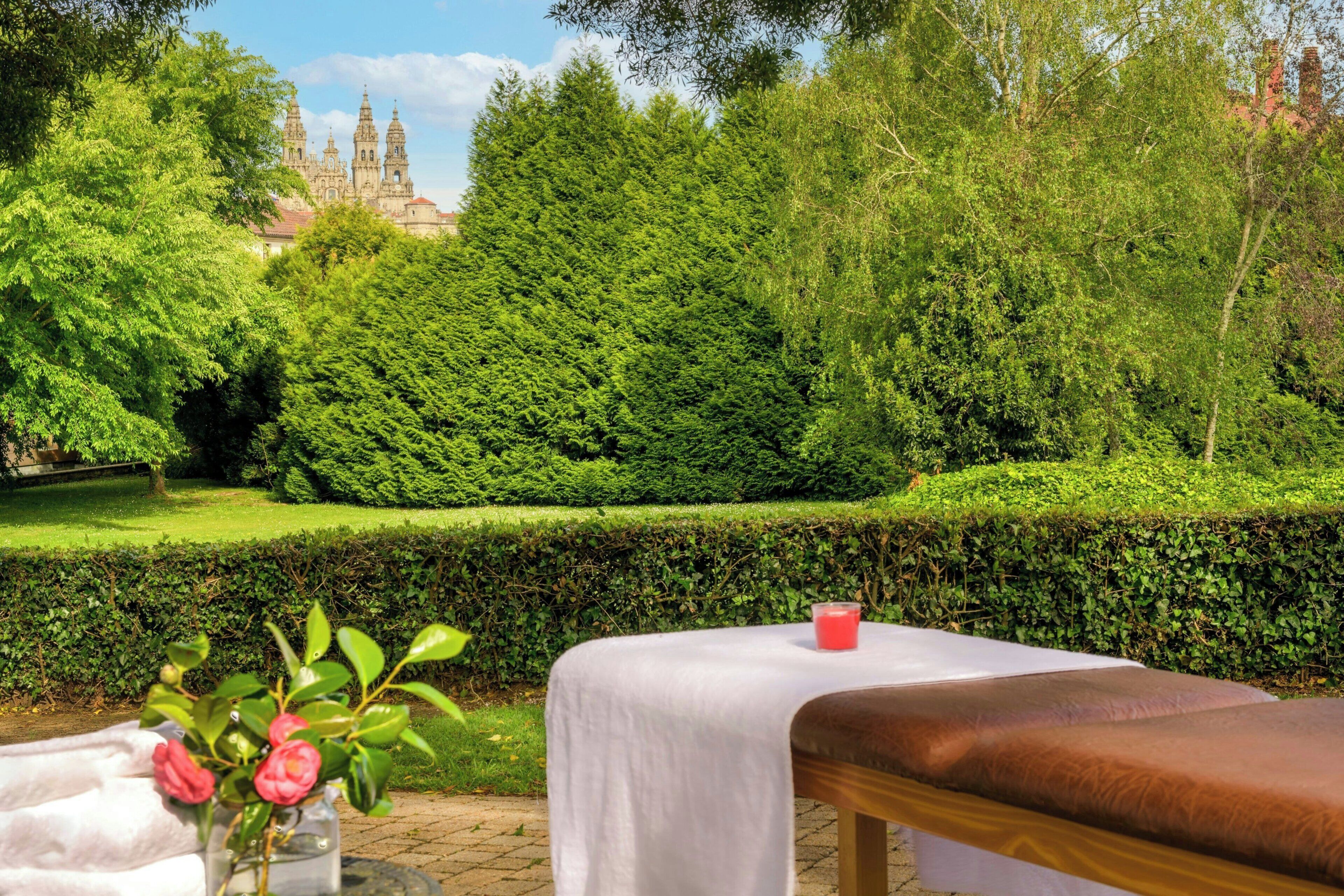 Un jardín con una mesa y banco, un jarrón de flores y una vista distante de un edificio histórico.