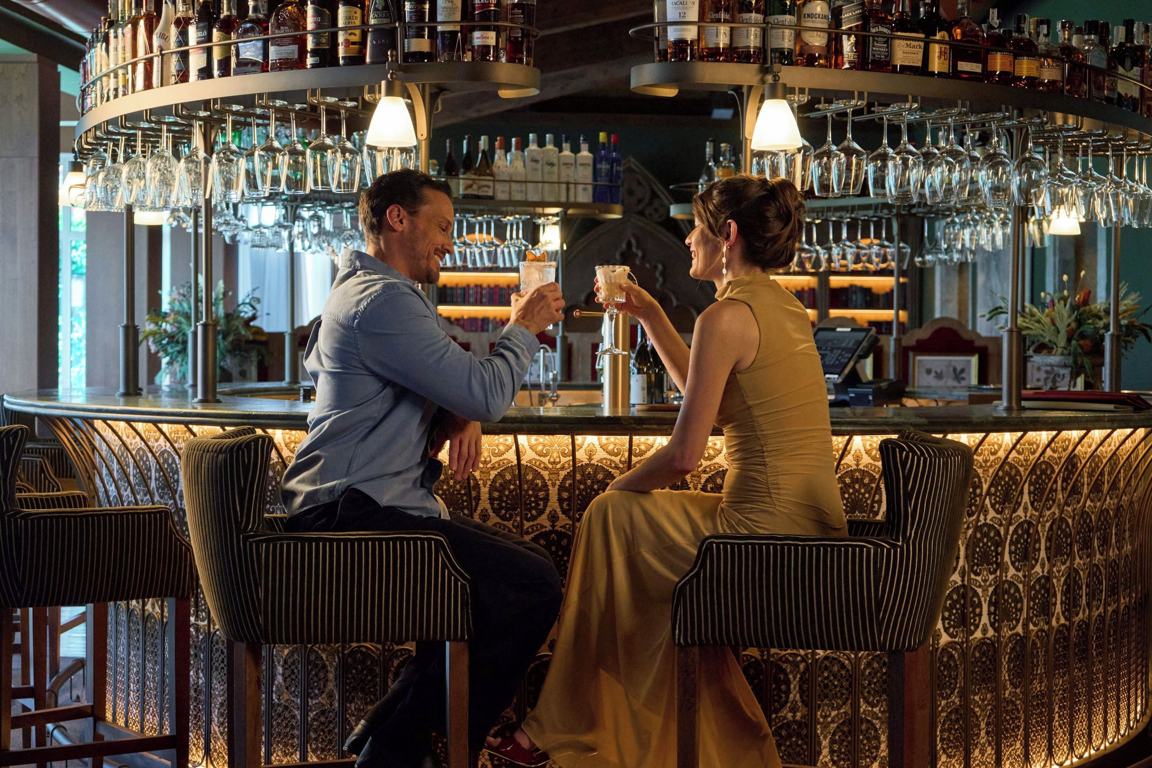 Um espaço de bar com balcão curvo, várias garrafas de bebidas e copos pendurados.