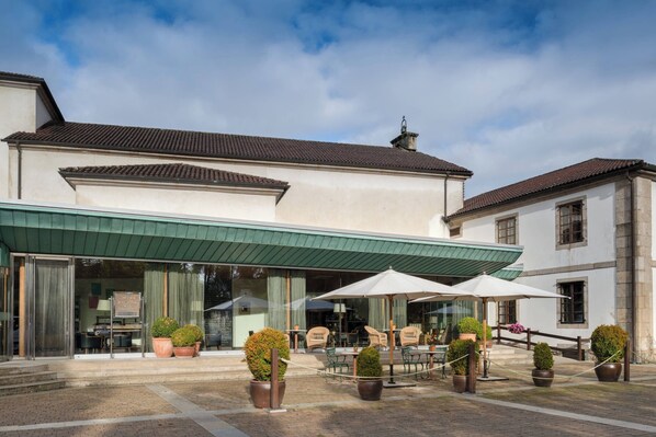 A hotel with a covered outdoor seating area, potted plants, and a brick-paved courtyard.