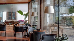 Un hall d’entrée spacieux, doté de fauteuils en cuir, d’une table basse en bois et de grandes fenêtres donnant sur l’espace extérieur aménagé en coin salon.