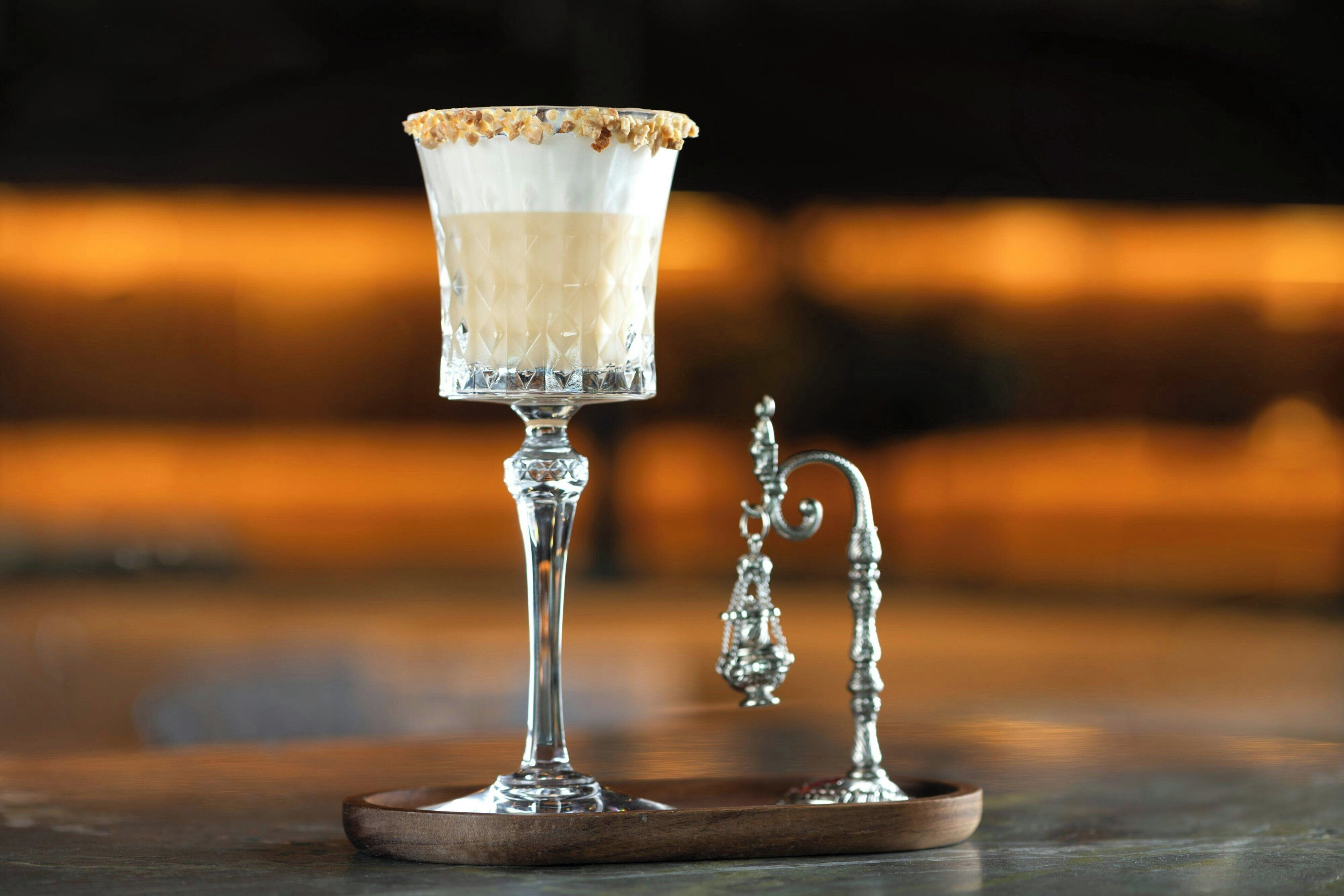 A glass with a layered drink, a metal tray, and a decorative metal piece on a wooden surface.