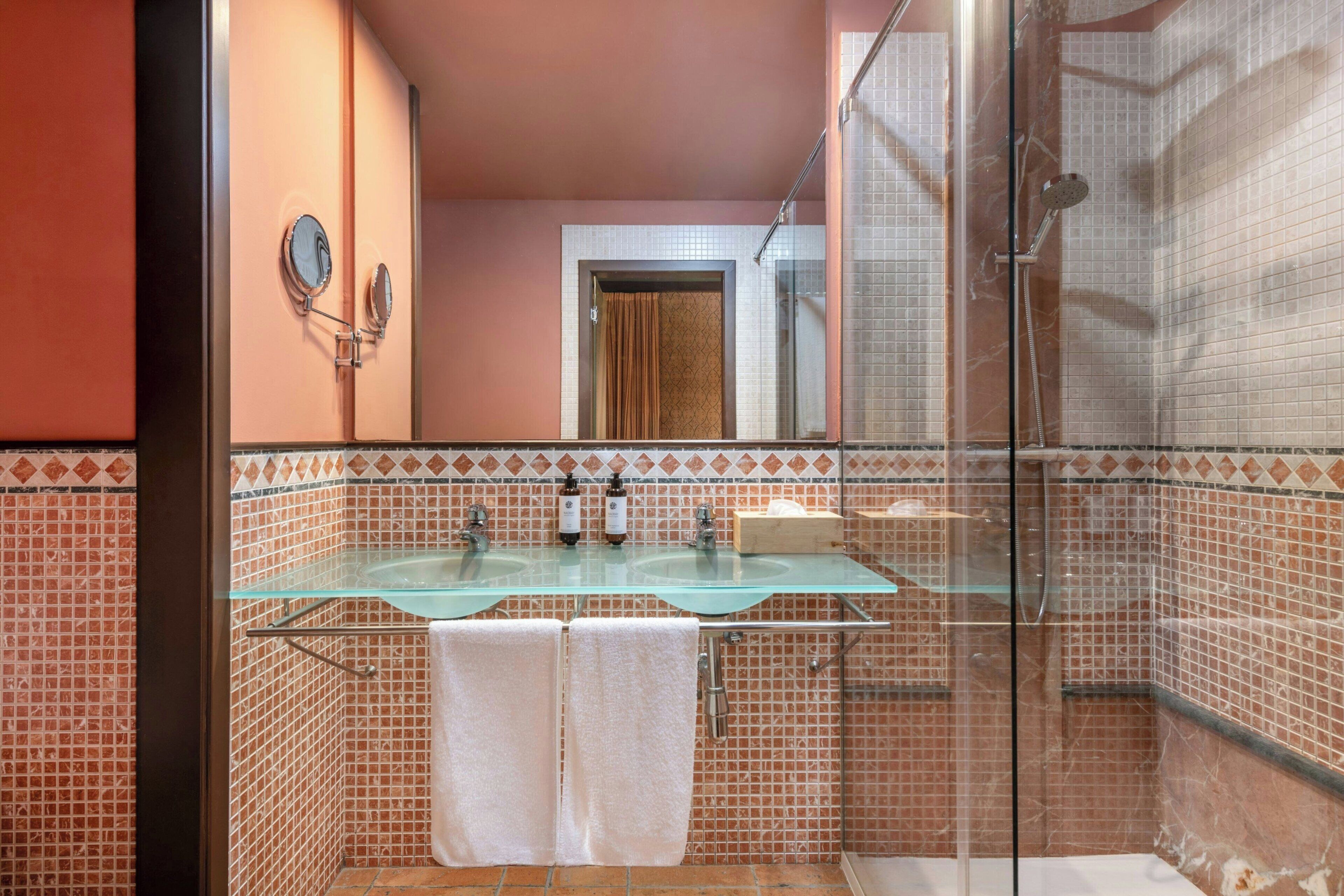 A bathroom with a glass sink, two white towels, a shower, and a mirror.