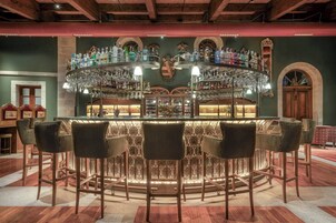 Zona de bar con barra circular, varios taburetes y una variedad de botellas y vasos.