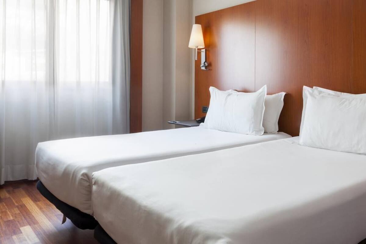 Una habitación de hotel con dos camas, cabecera de madera, mesita de noche y una lámpara.