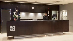 A reception desk with a dark wood finish, a logo indicating it's part of a hotel chain, and a digital screen. - Hotel Ciudad de Lleida (Lleida)